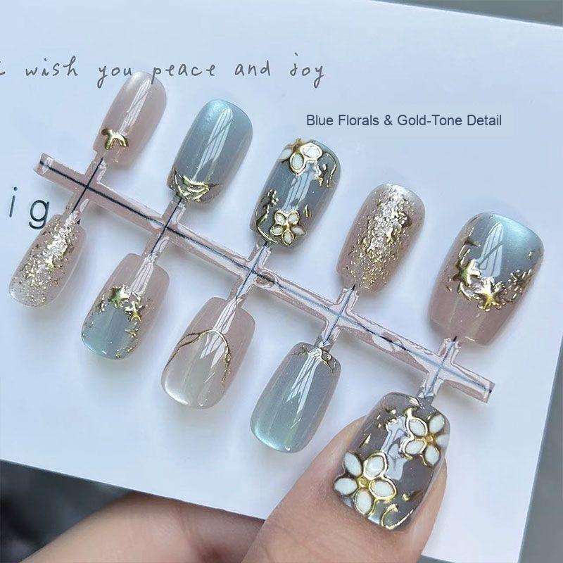 Close-up of blue floral press-on nails with gold-tone accents